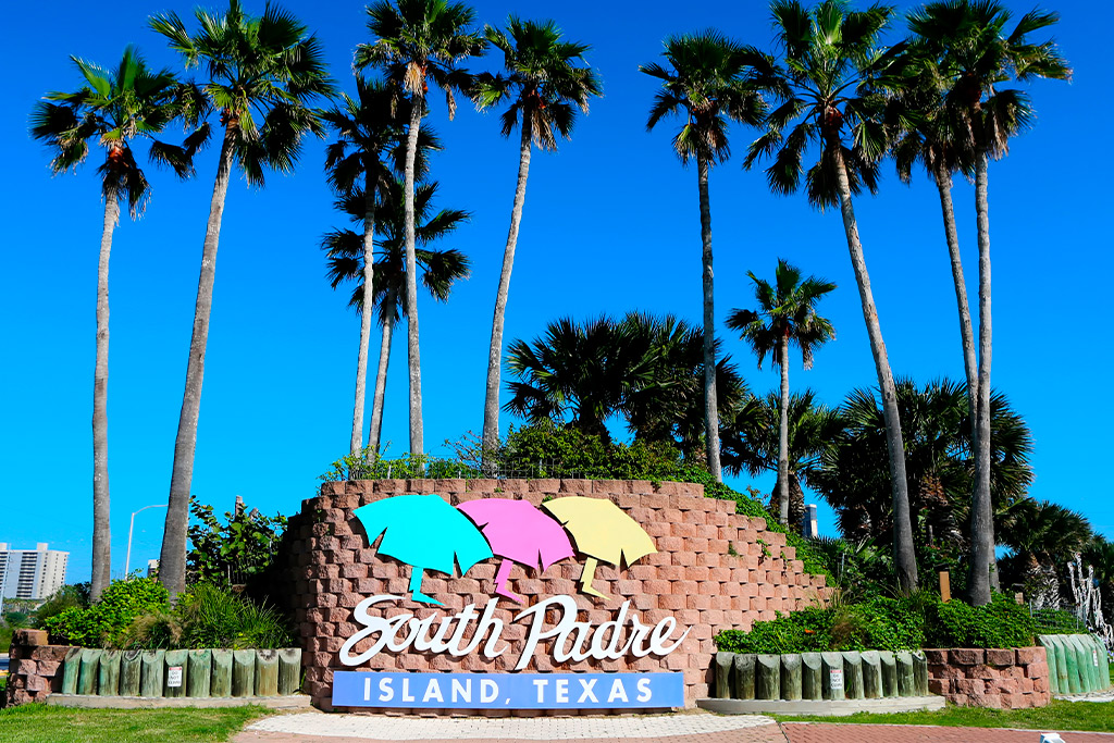 Beach resort sign in front of lush palm trees, perfect for family travel in the RGV area. South Padre Island. 