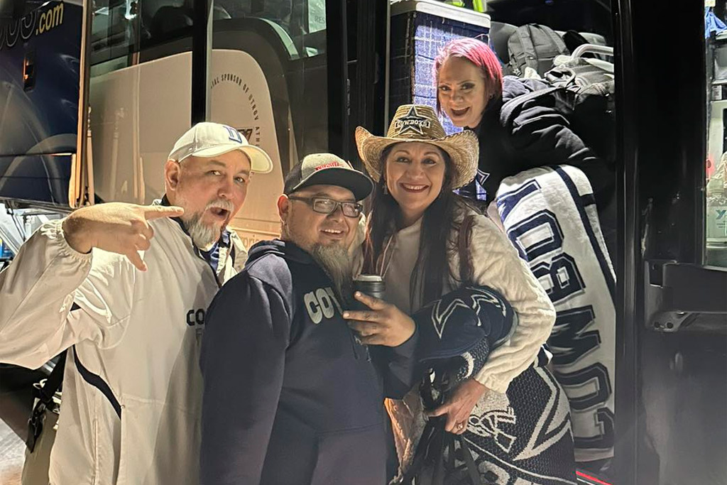 A family smiles for a photo in front of a bus, celebrating their day at the AT&T Stadium for the RGV Cowboys game.