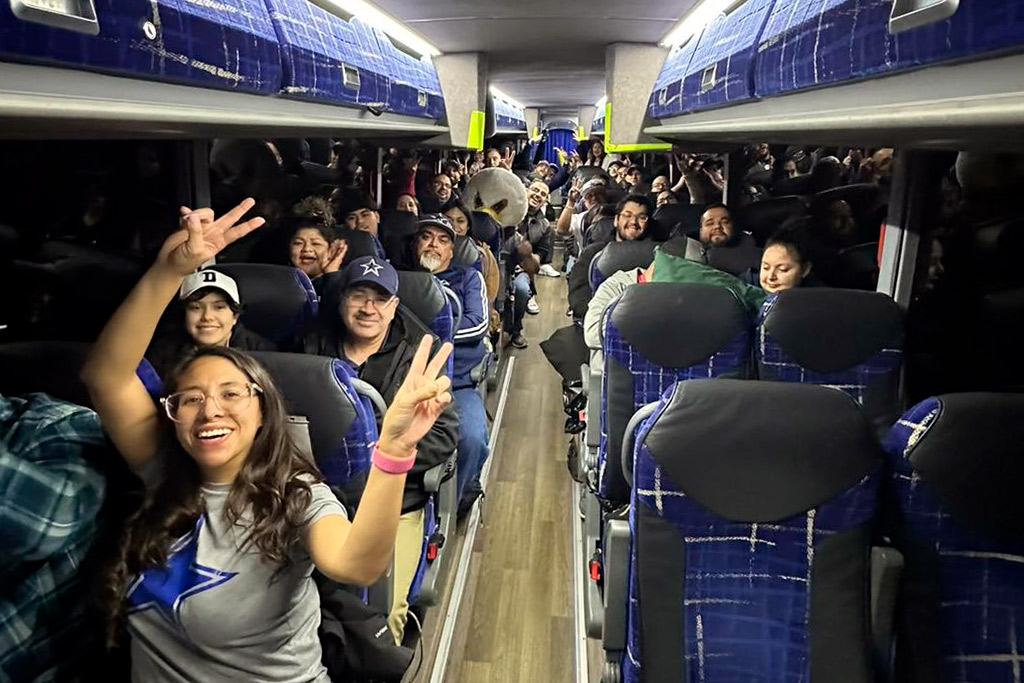 Enthusiastic fans on a bus, hands up in celebration, gearing up for the RGV Cowboys game at AT&T Stadium.