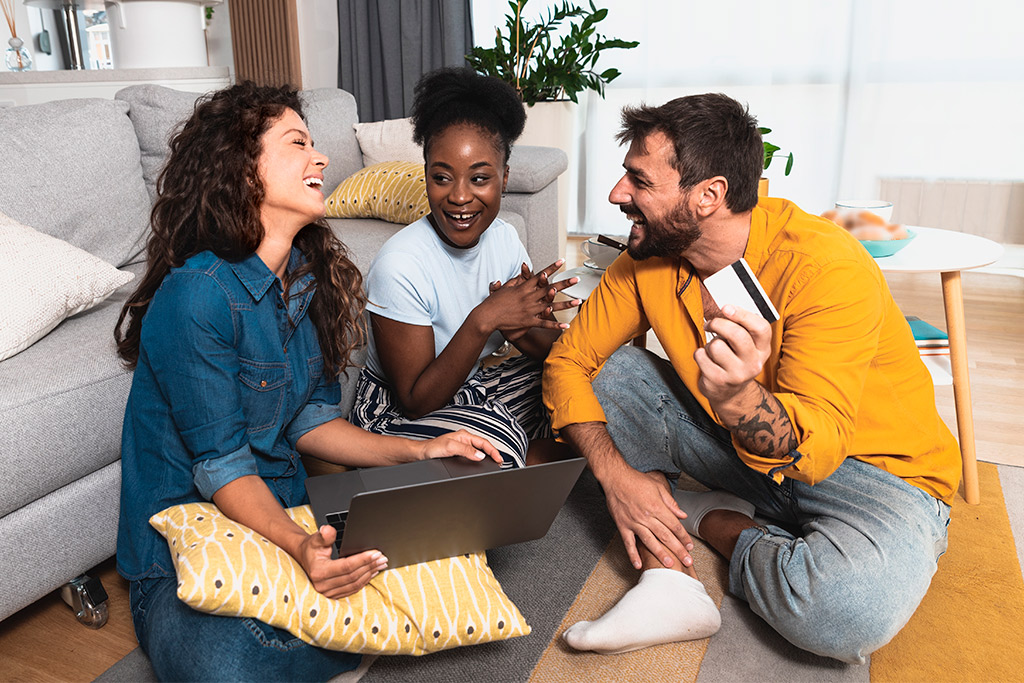Three individuals on the floor with a laptop and credit card, discussing their upcoming casino trip.